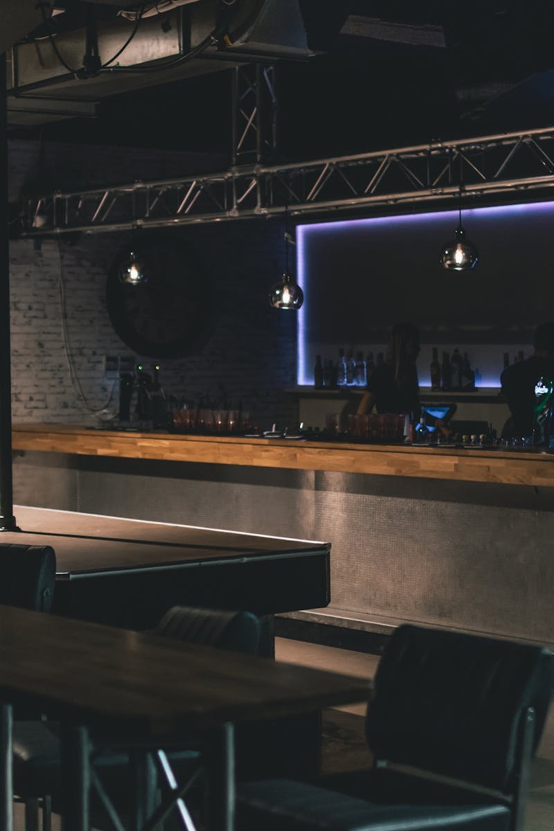 Stylish modern nightclub interior featuring a sleek bar counter with ambient lighting and industrial design elements.